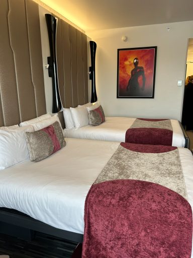 A hotel room featuring two double beds with decorative cushions and a framed artwork on the wall.