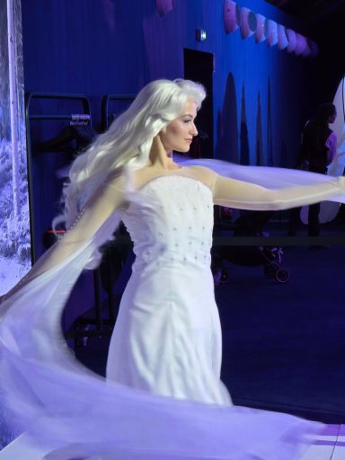 Elsa, in a flowing white gown with long, blonde hair, gracefully posing.