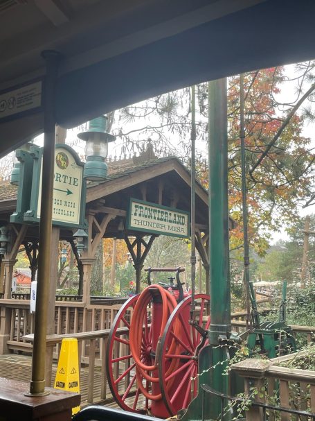 A red hose reel in a rustic outdoor setting with wooden structures and autumn foliage.