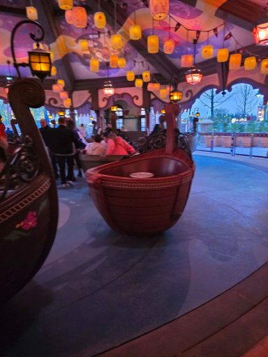 Ride vehicle Interior of an amusement park attraction with wooden boats and glowing lanterns.