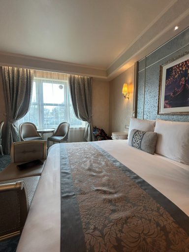 Luxurious hotel room with a large bed, armchairs, and elegant decor by the window.