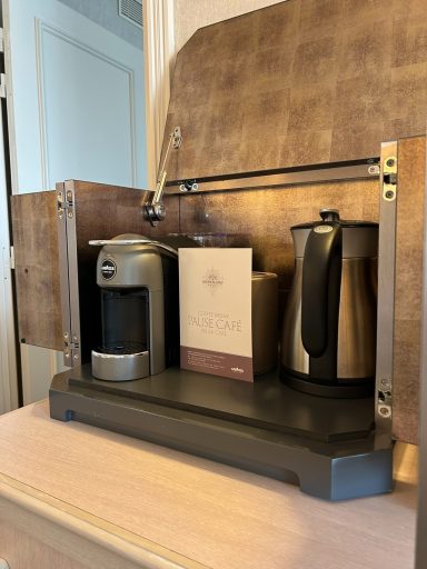 Coffee station featuring a coffee machine, kettle, and a box on a wooden surface.