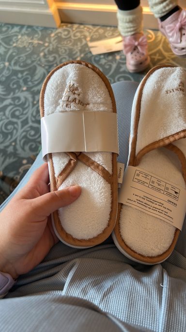 A person holding a pair of white spa slippers with a comfortable design.
