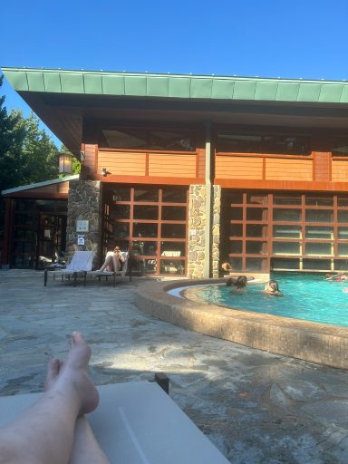 A person relaxing by a poolside with a wooden building in the background.