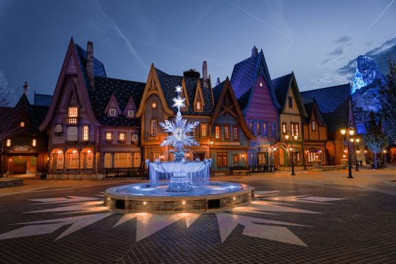 Charming village square at dusk featuring a central fountain and colourful buildings.