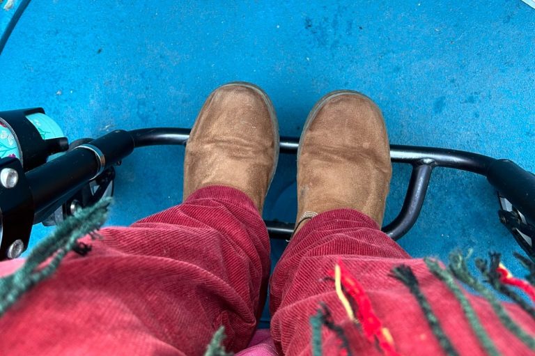 Image of feet on a wheelchair footplate with the blue ride vehicle floor visible