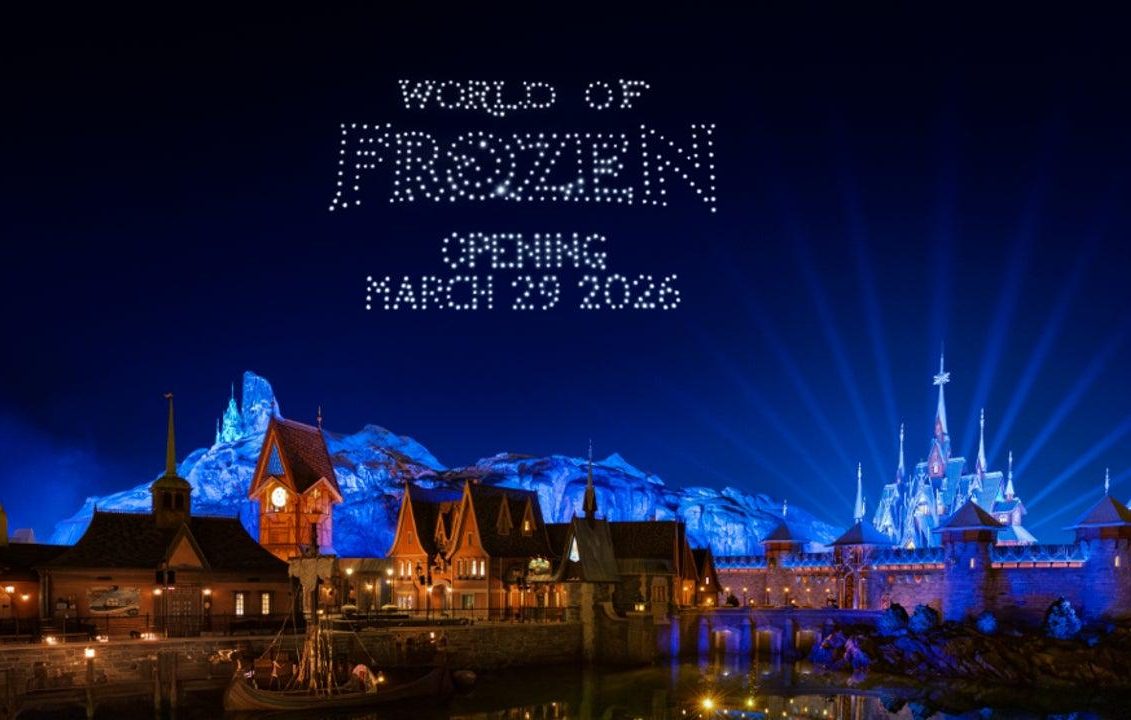 Nighttime scene of a Frozen-themed amusement park with illuminated buildings and mountains, promoting the opening.