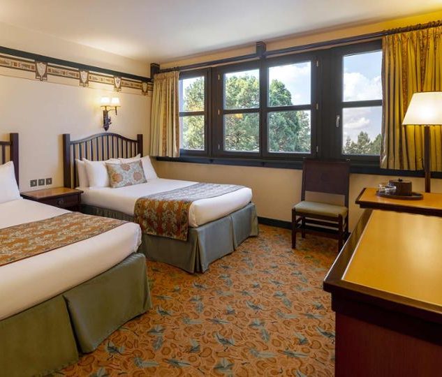 Image of a standard room showing 2 double beds, a tv, dresser, and woodland theming with muted colours and dark wood windows and furniture