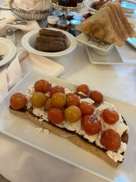 Plate with a dessert topped with cream and assorted small fruit, alongside toast and sausages.