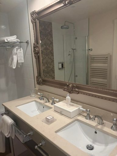 Elegant bathroom with double sinks and a large ornate mirror. Towels are hanging nearby.