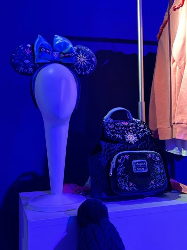 Minnie Mouse ears on a stand next to a backpack, displayed in blue lighting.