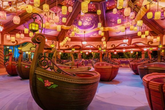 Colourful indoor setting with illuminated lanterns and whimsical boat ride vehicles.