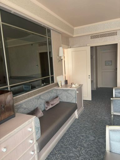 A spacious hotel room with a seating area, mirror, and doorway to another room.