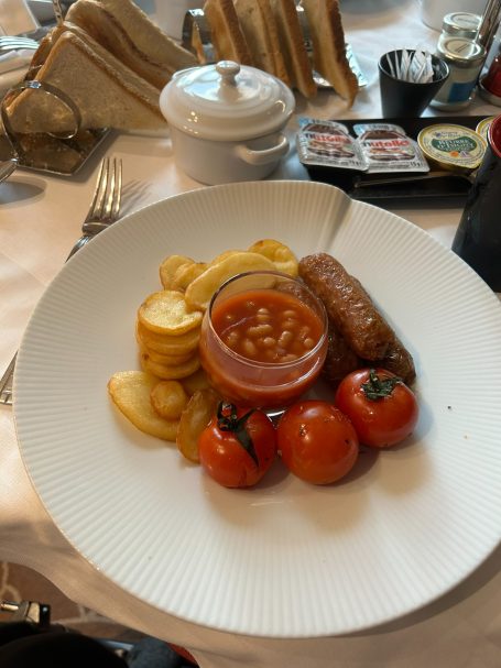A plate with sausage, baked beans, tomatoes, and sliced potatoes.