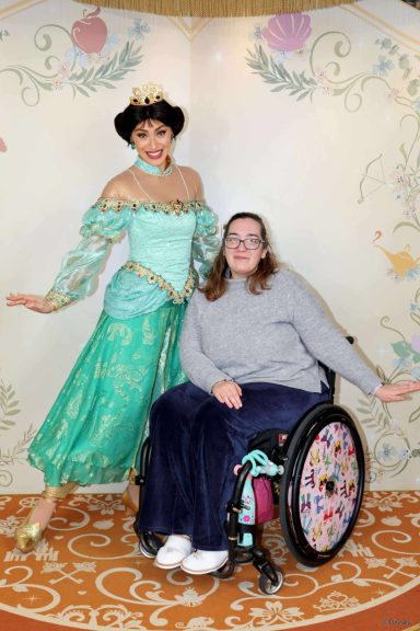 A girl in a wheelchair poses with a woman dressed as a princess in a decorated setting.
