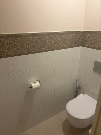 Modern bathroom with white tiles, decorative border, and a toilet with toilet paper.