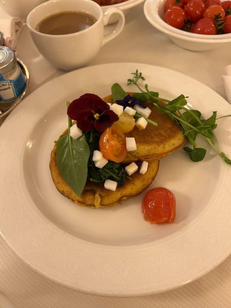 Fluffy pancake topped with greens, cherry tomatoes, cheese, and edible flowers, served with coffee.