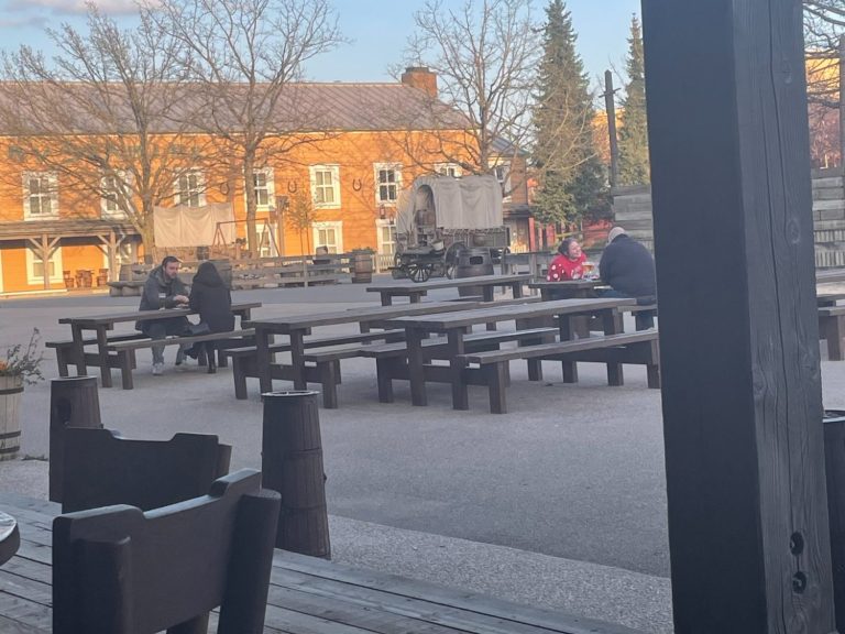 People sitting at outdoor wooden tables in a sunny courtyard.