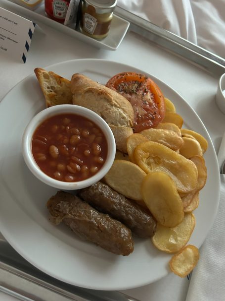 A plate featuring sausage, baked beans, sliced tomato, and crispy potato chips.