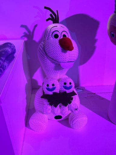 Olaf the snowman toy holding two smaller snowman toys against a purple background.