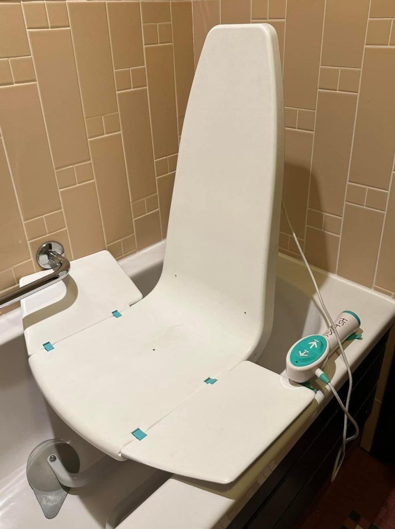 Image of a bath seat used in a standard bath, it is white and fits within the bath and can rise up to transfer to bath