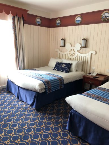 A hotel room with two beds, patterned carpet, and coastal-themed decor.