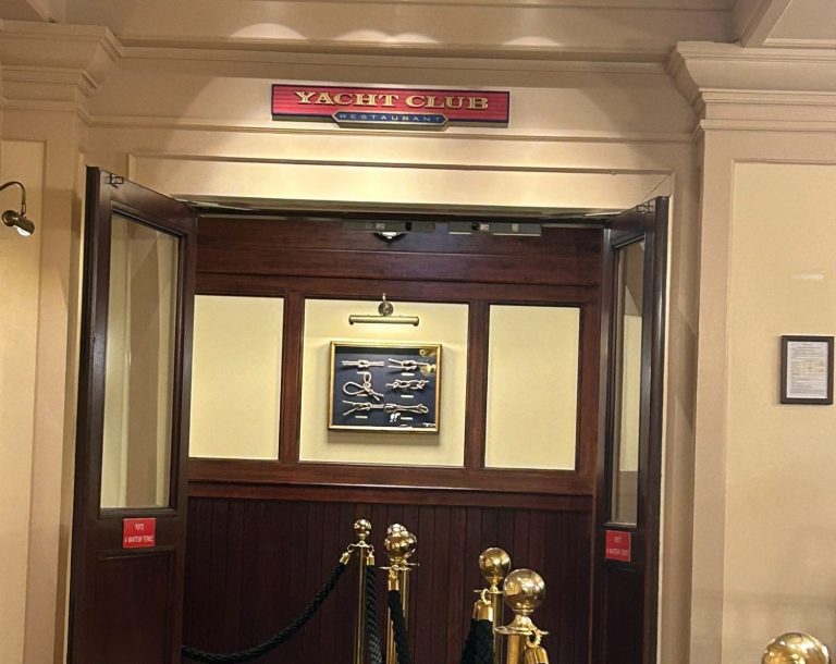 Entrance to a room with a sign reading “Yacht Club” and gold stanchions.