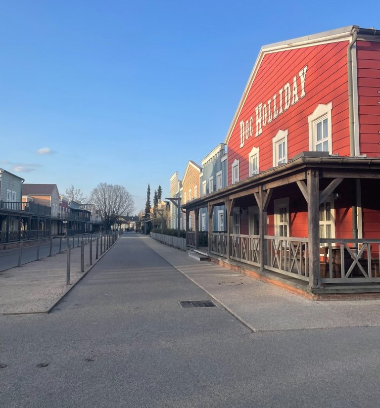 Quiet street scene with a red wooden building on the left and clear blue sky.