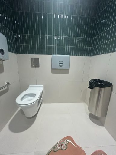 Clean bathroom with a toilet, bin, and paper towel dispenser against green tiled walls.