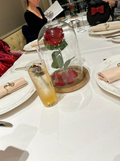 A glass cloche with a rose, surrounded by a dining setting with drinks and napkins.