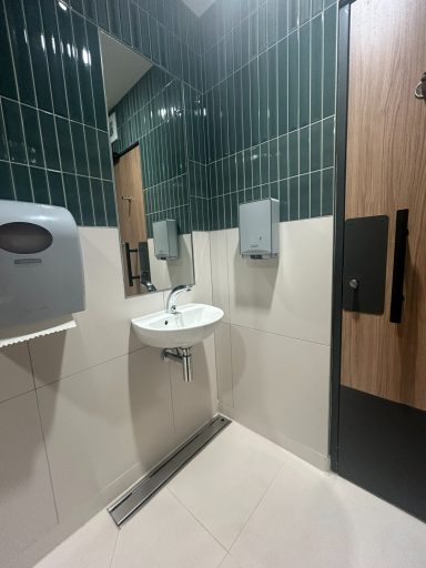 Clean restroom with a sink, soap dispenser, and green tiled walls.