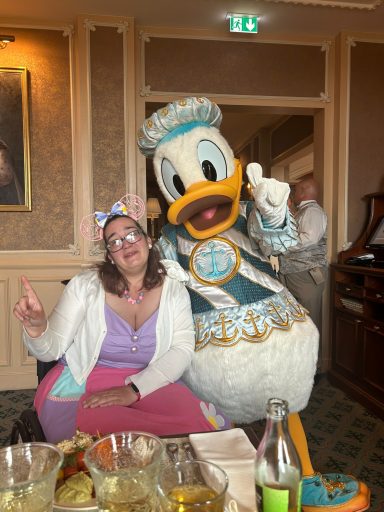 A woman in festive attire poses with a character dressed as Donald Duck.