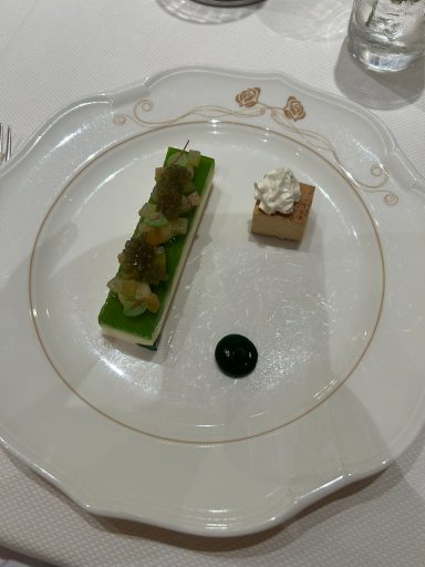 Dessert plate featuring green dessert with toppings and a small cake, garnished with sauce.