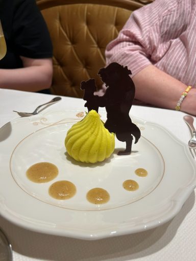Yellow dessert with chocolate silhouette figures and sauce dots on a white plate.