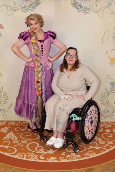 A woman in a wheelchair poses with a character dressed as Rapunzel.