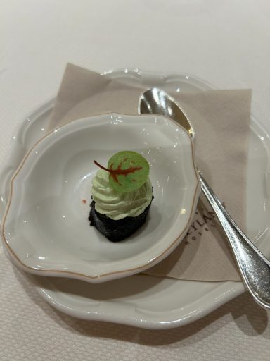 A small dessert topped with mint green cream and a decorative leaf on a white plate.