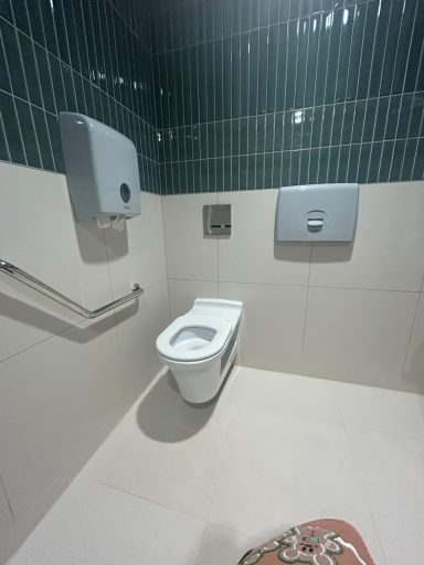 A clean bathroom stall with a toilet, hand dryer, and grab rail on tiled walls.