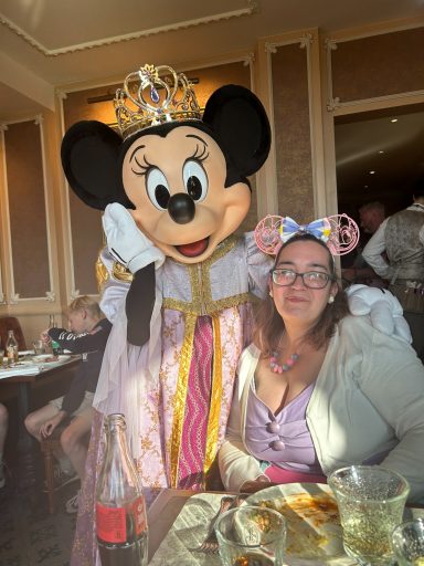 Minnie Mouse in a dress poses with a smiling woman wearing ears at a restaurant.