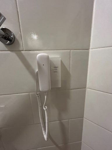 A white telephone mounted on a tiled wall near a shower.