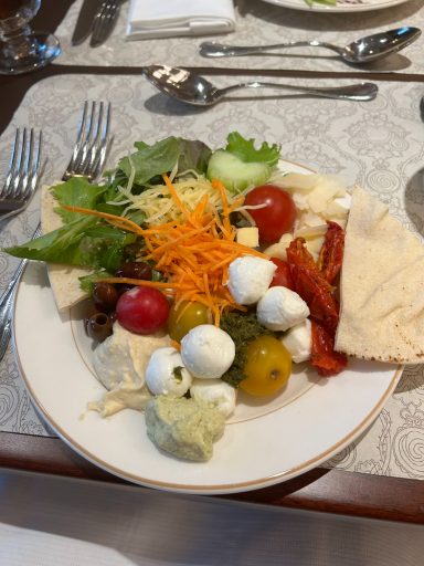 A plate of colourful salad with mixed greens, tomatoes, cheese, and pita bread.