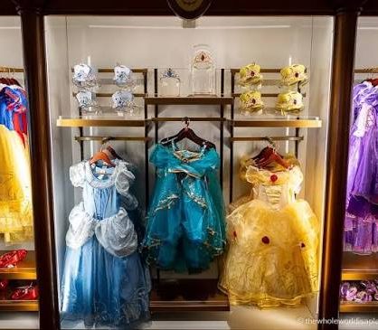 Children's princess costumes displayed in a wooden wardrobe, featuring blue and yellow dresses.