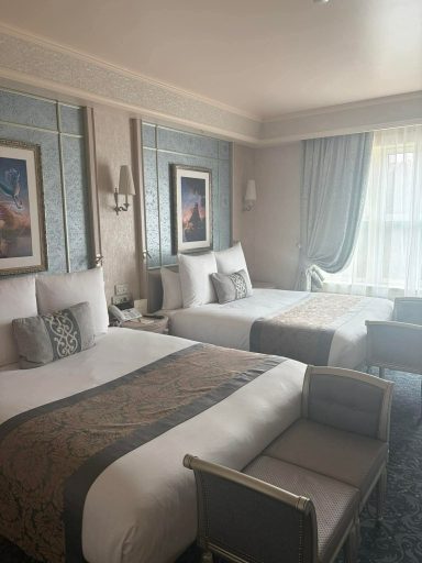A stylish hotel room with two beds, elegant decor, and large windows.