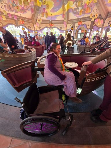 Side transfer into vehicle A woman in a wheelchair sits beside a carousel ride, with colourful decorations in the background.